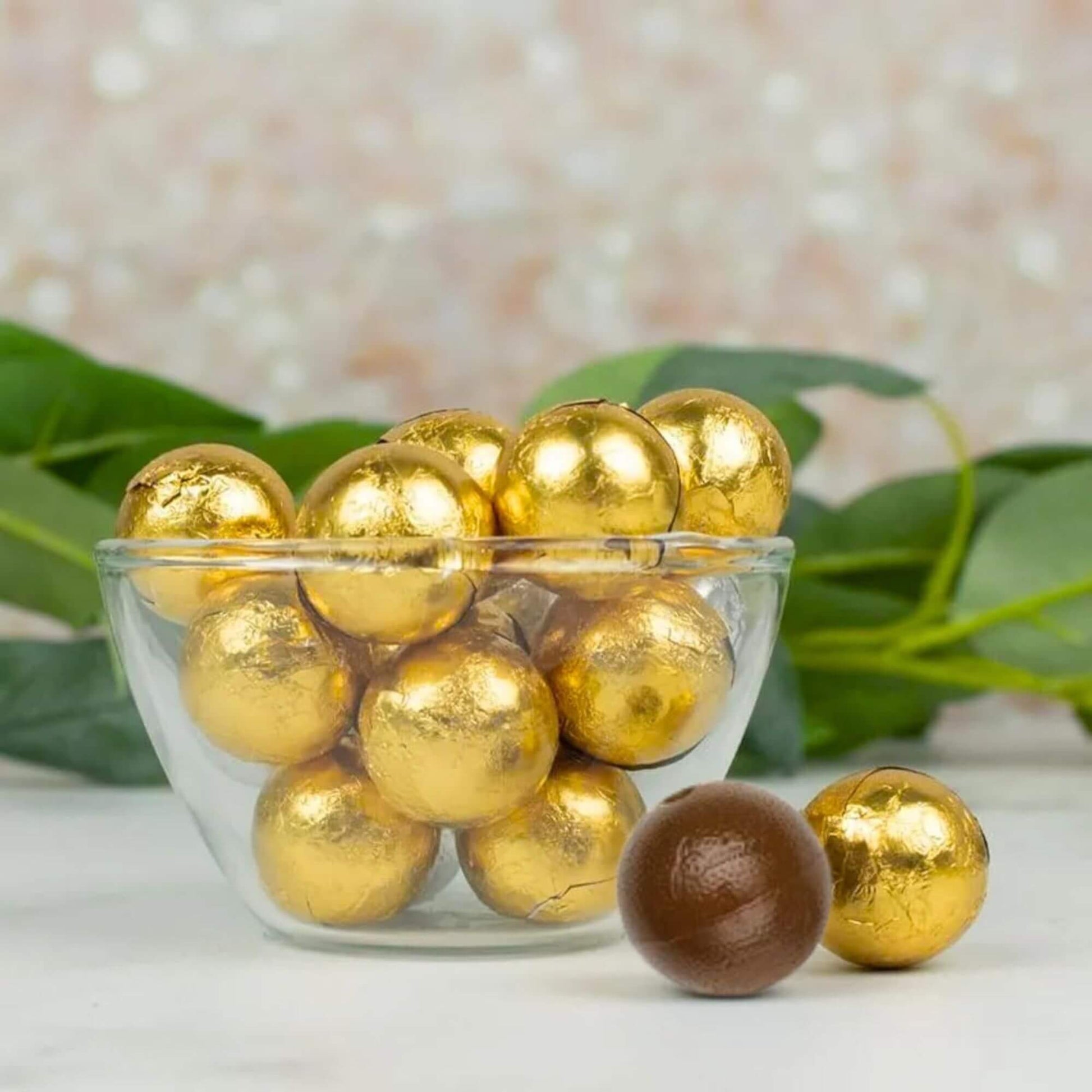 Glass bowl filled with gold-wrapped chocolates on a light background