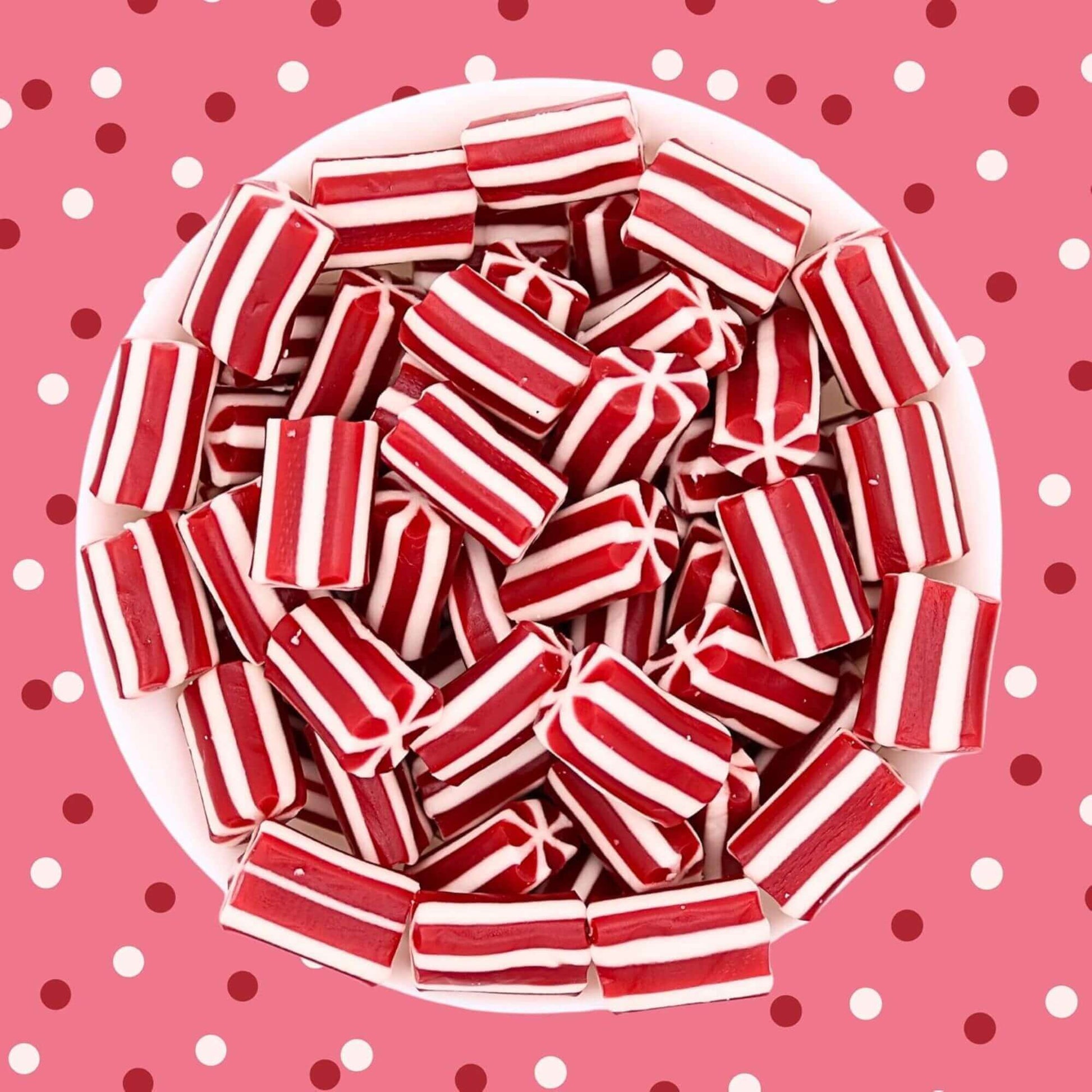 Red and white striped candies in a white bowl on a pink polka dot background