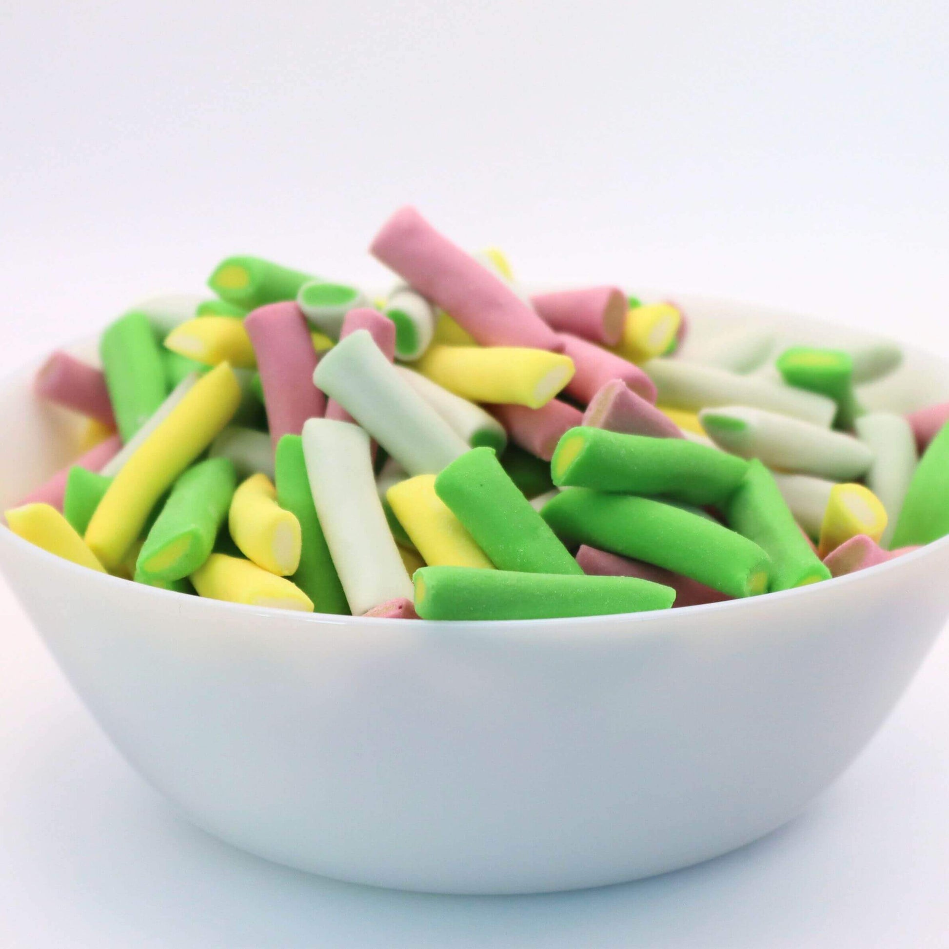Colorful licorice sticks in a white bowl on a light blue background